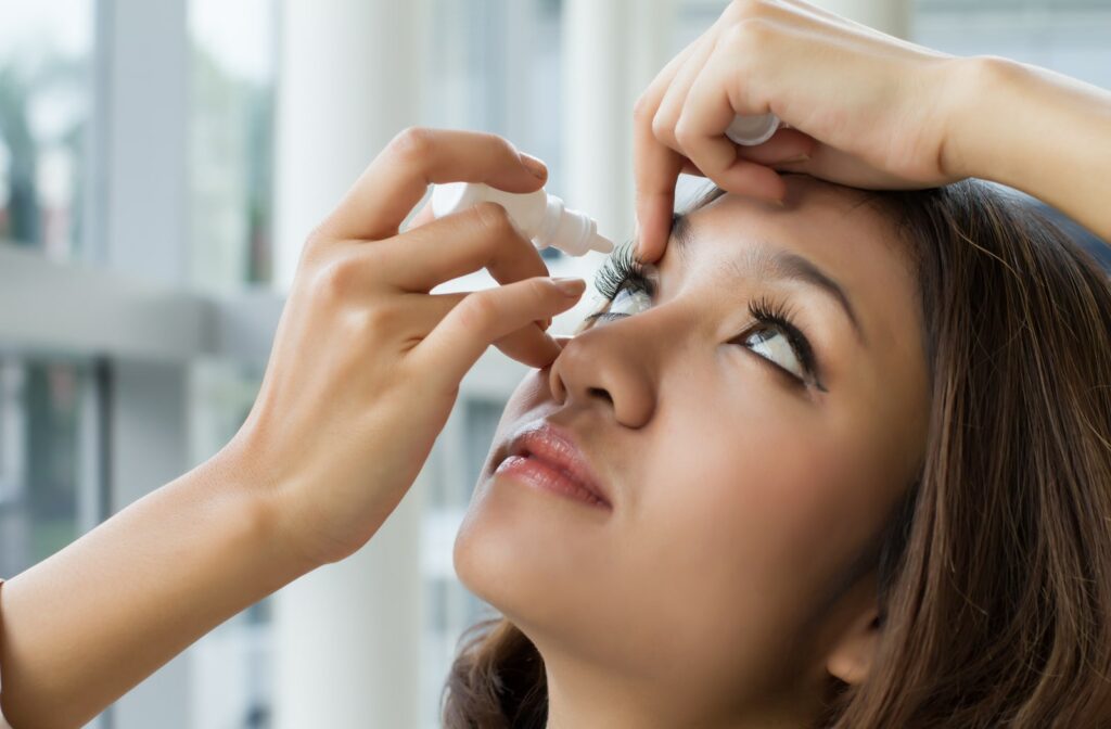 A woman putting eye drops into her right eye