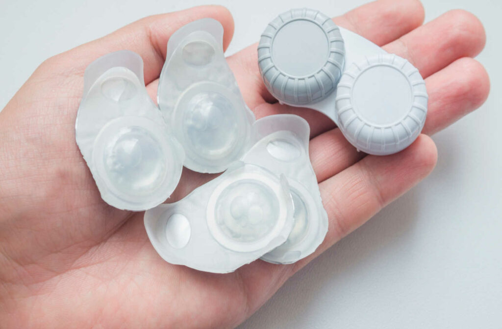 A close up of a hand holding a contact lens case and contact lens blister packs.