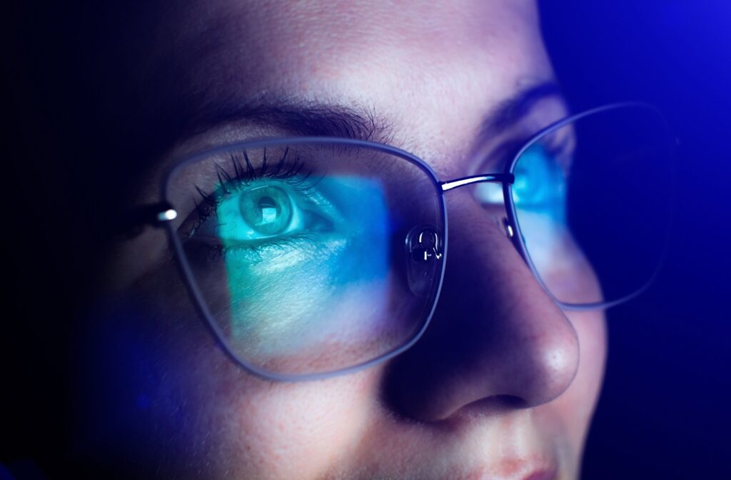 A close up of a person wearing blue light glasses with the digital screen reflecting off the lenses.
