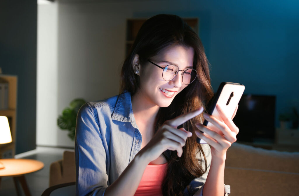 A woman wearing blue light glasses while looking at her phone to protect her eyes from digital eye strain.