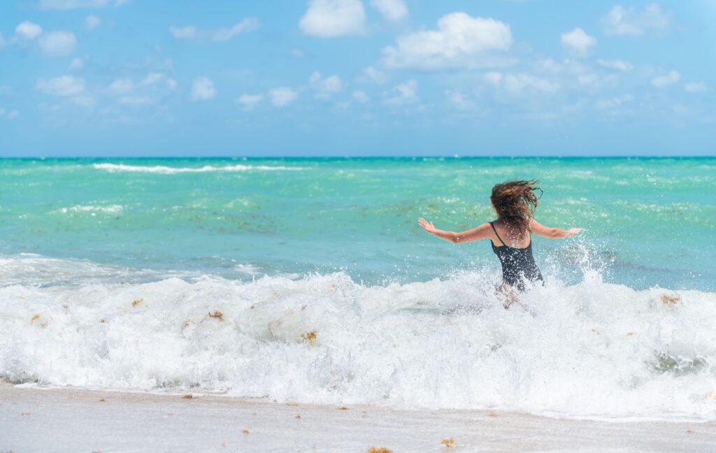 A person runs across a white sand beach and into crystal clear, blue water.