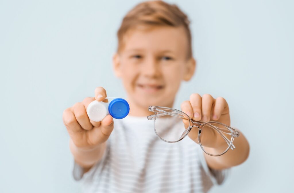 A child holding out a pair of glasses in one hand and contact lenses in the other hand, displaying the options of myopia control in San Clemente.
