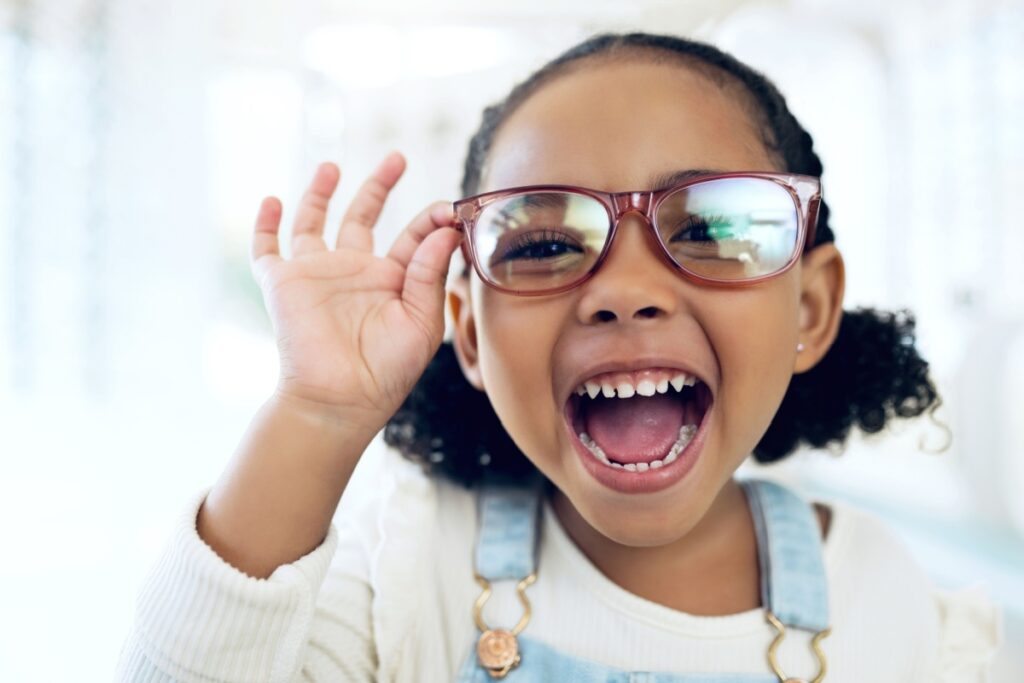A child smiling holding a pair of glasses on their face.