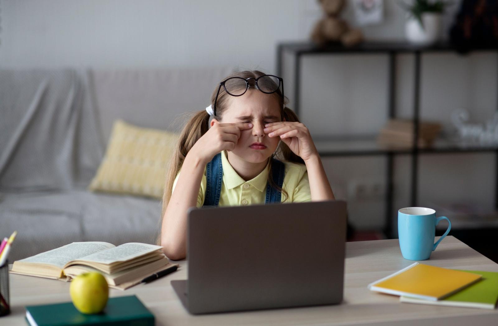 A child rubbing their eyes after looking at a laptop screen for a prolonged period of time.